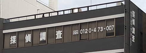 津市のビル上階の窓に表示された探偵調査の文字