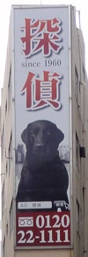 新宿二丁目交差点で撮影された黒い犬の探偵看板